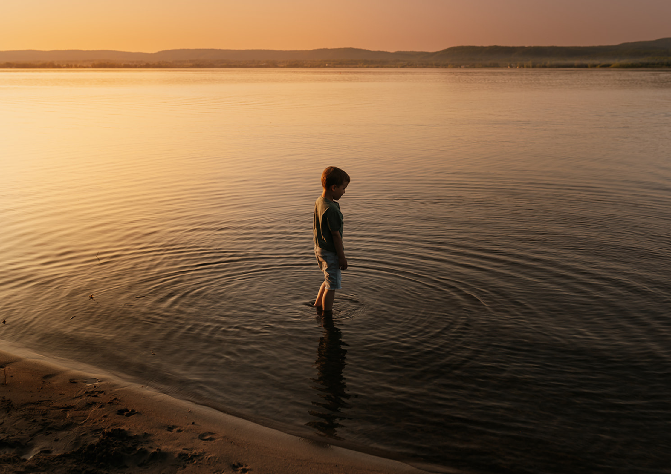 a boy at sunset dipping his feet into the Ottawa river in Constance Bay